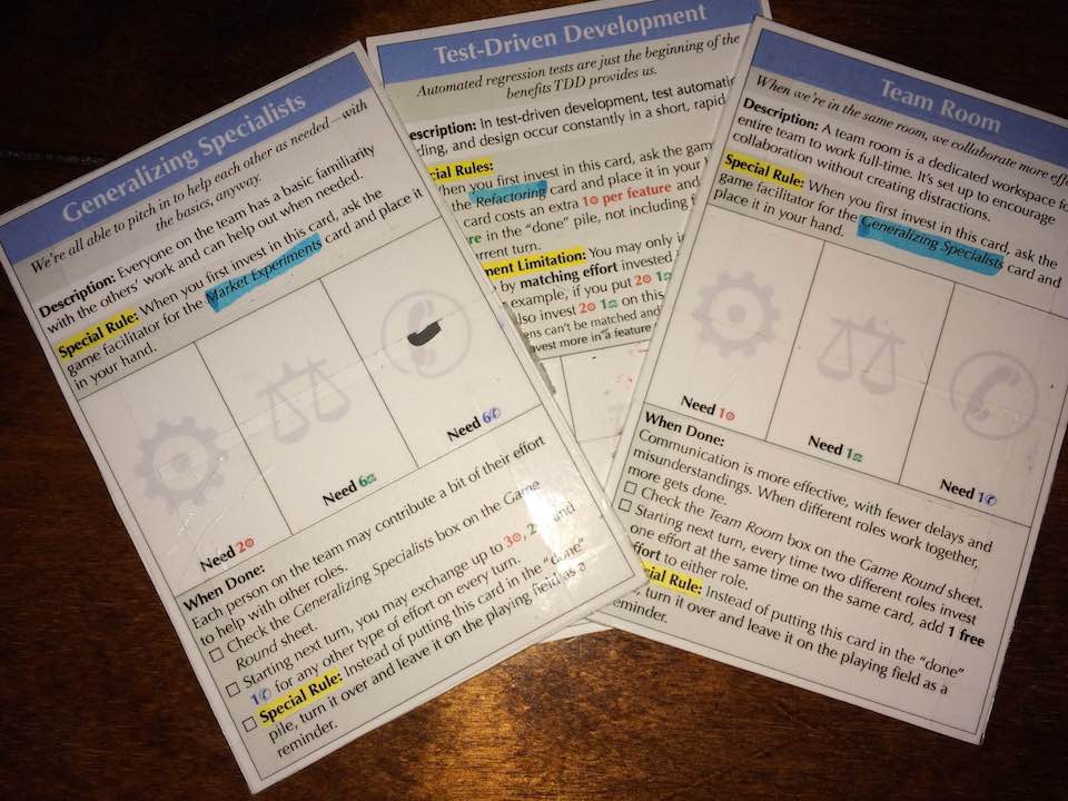 Picture of an three game cards. They show dense text with three places in the middle for putting game tokens.