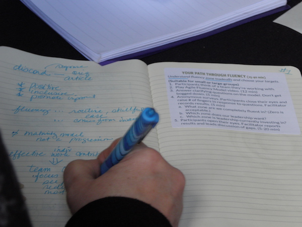 Closeup of a workshop participant writing on a notebook page, with a sticker on the other page